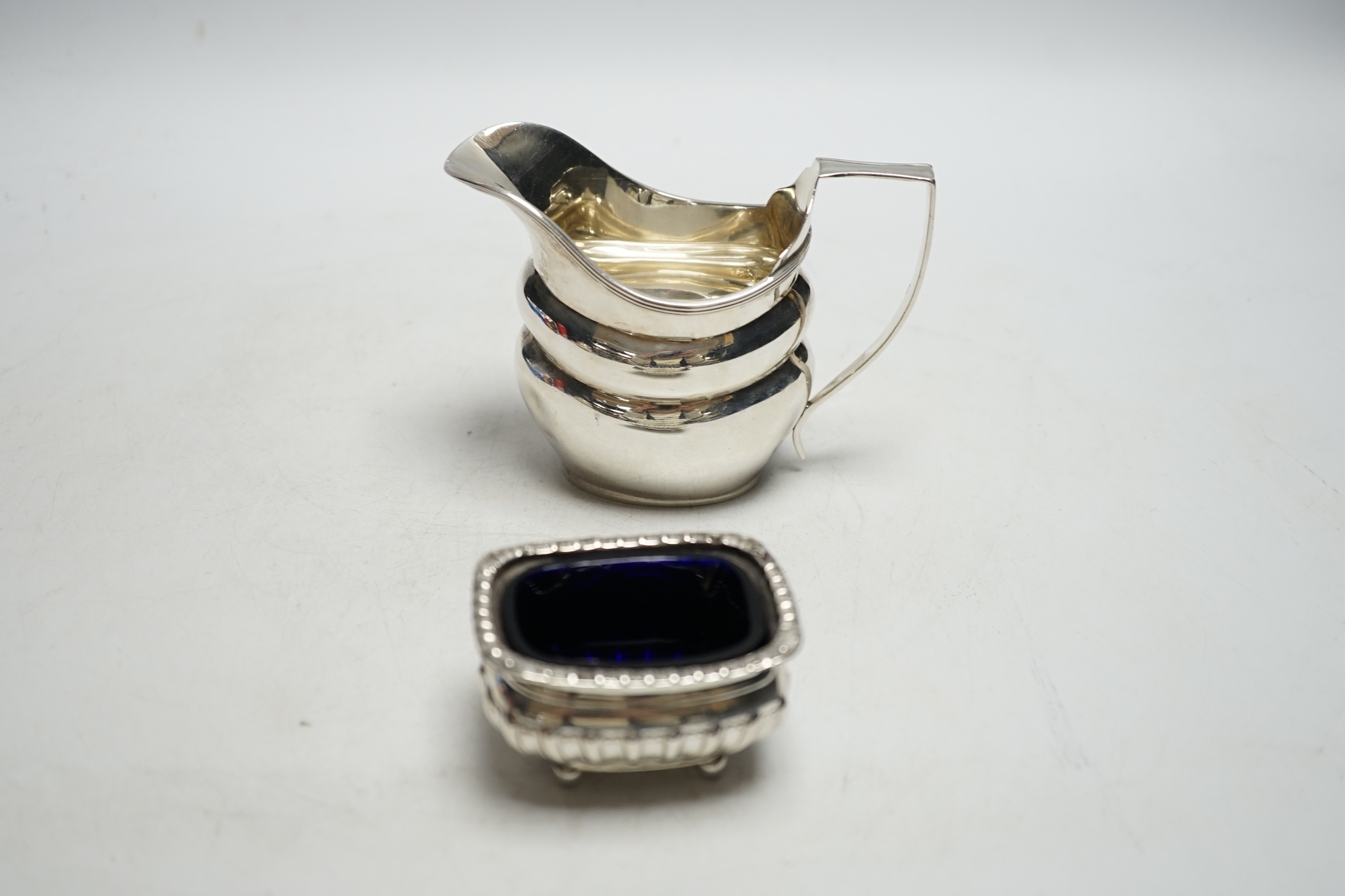 A George V silver helmet shaped cream jug and a silver salt with a gadrooned border.